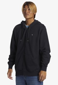 Sort zip-up hoodie lavet af blødt stof, med en hætte med snor, forlommer, ribbede manchetter og et lille logo på brystet.