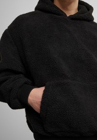 Felpa con cappuccio in pile nero con esterno morbido e strutturato, grande tasca frontale e polsini a coste. Presenta un ampio cappuccio per una maggiore copertura.