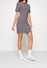 Robe à manches courtes rayée en marine, rose et blanche, avec un col rond rouge. Texture douce avec un ourlet droit au niveau des cuisses.