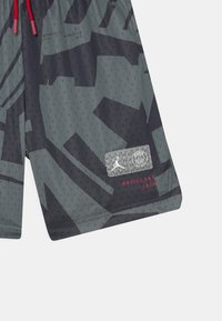 Harmaat shortsit, joissa on musta abstrakti kuvio, reikärakenne, joustava vyötärö, jossa on punainen nyöri, sekä brändäysliima, jossa on logoja ja numeroita.