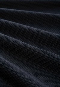 Donkere, gestructureerde stof met een geweven patroon, voorzien van verhoogde hexagonale vormen, die een golvende uitstraling over het materiaal creëren.