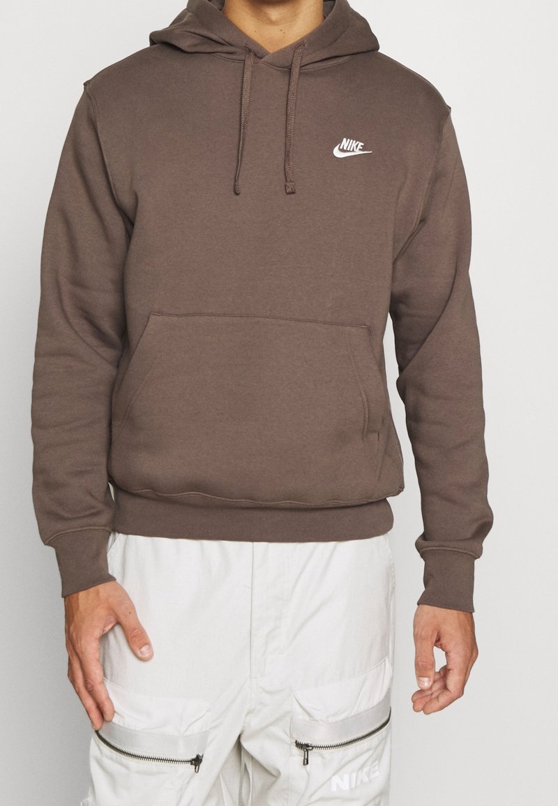 Brun huvtröja i mjukt material, med en framficka, ribbade muddarna och en vit Nike-logga på bröstet.