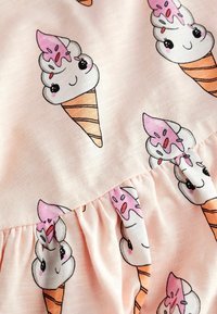 Tissu rose clair avec des cornets de glace dessins animés affichant des visages souriants, des garnitures roses et des cornets gaufrés en motif répété.