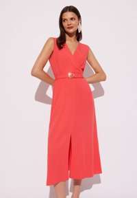 Korallowa, bezrękawnikowa sukienka z dekoltem w kształcie litery V i paskiem w talii z metalową klamrą. Sukienka do połowy łydki z detalem rozcięcia z przodu. Gładka faktura materiału.