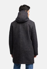 Wool blend coat in dark herringbone with a hood, featuring a textured surface and straight cut, worn over blue jeans.