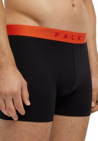 Boxer neri con un elastico arancione in vita che presenta la scritta "FALKE" in rosso. Il materiale sembra liscio e aderente.