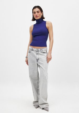 Maglione a collo alto a coste in blu vivace, abbinato a jeans grigi sbiaditi e a gamba larga e tacchi grigi a punta. Look minimalista nel complesso.