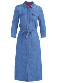 Pitkänsininen farkkuasu, jossa on kaulus, napitettu rintataskuja, kolmannes-pituiset hihat, etunapit ja samaa kangasta oleva vyö solmittuna vyötärölle.