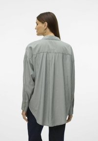 Camicia a righe verde chiaro e bianca, con maniche lunghe, colletto e vestibilità relax. Il tessuto appare liscio con una leggera lucentezza.