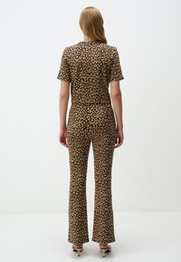 Set a due pezzi con stampa leopardata in marrone e beige, composto da un top aderente a maniche corte e pantaloni svasati dal texture morbida.