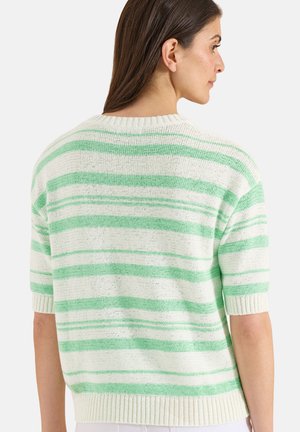 Femme aux longs cheveux bruns portant un pull en tricot blanc avec des rayures horizontales vert clair, vue de dos et de profil.