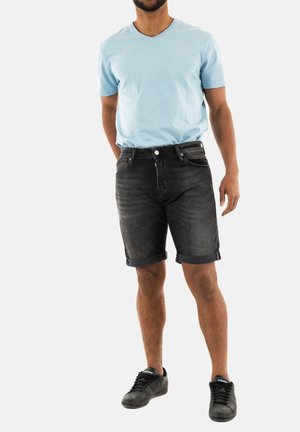 Shorts de mezclilla negra con dobladillos enrollados, con cierre de botón en la parte delantera. Combinados con una camiseta de cuello en v de color azul claro y zapatillas negras.
