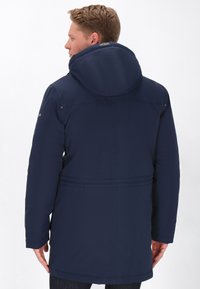 Námornícky modrá vonkajšia bunda s kapucňou, vyrobená z hladkej tkaniny. Má opaskový pás a jemné detaily šitia.