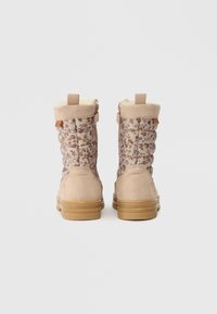 Beige színű téli csizma pár, virágmintás steppelt anyaggal, velúr sarkakkal és húzófülekkel, hátról nézve, fehér háttér előtt.