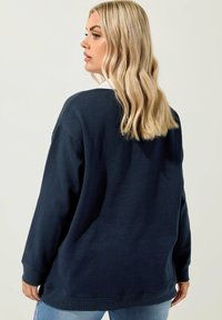 Marinblå oversized sweatshirt i mjukt material, med rund halsringning, långa ärmar och ribbade muddar. Bakre vy visas.