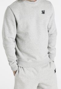 Sudadera gris hecha de una mezcla de algodón, con cuello redondo, puños de canalé y un pequeño logo negro en el pecho.