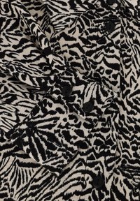 Zwart-witte dierenprint stof met een gestructureerd oppervlak, voorzien van vier ronde zwarte knopen en een opstaande kraag.