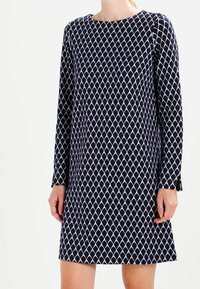 Dunkelblaues Langarmkleid mit einem weißen Diamantmuster. Es hat einen Rundhalsausschnitt und einen geraden Schnitt und besteht aus einem glatten Stoff.