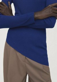 Modra rebrasta pletena majica z asimetričnim robom, združena z bež hlačami. Poudarek na teksturi in kontrastu barv.