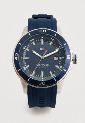 Meeste sinine Tommy Hilfiger käekell kummirihmaga, hõbedane korpus, kuupäevanäidik ja veekindel kuni 5 baari, näidates kellaaega 10:10:35.