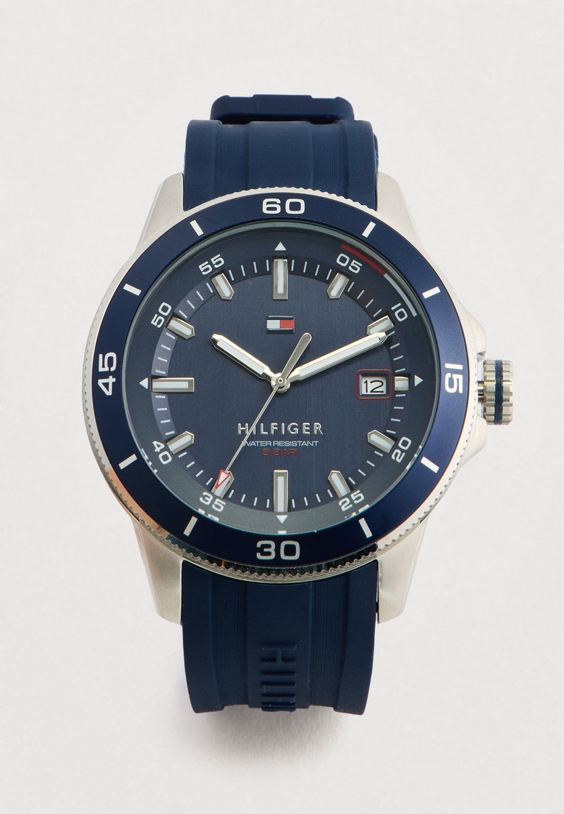 Ανδρικό μπλε ρολόι Tommy Hilfiger με καουτσούκ λουρί, ασημένια θήκη, ένδειξη ημερομηνίας και αντοχή στο νερό έως 5 μπαρ, που δείχνει 10:10:35.