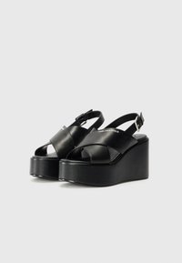 Sandali con plateau neri, dotati di ampie cinghie incrociate, design slingback e tacco a zeppa chunky. Realizzati in pelle liscia con una finitura lucida.