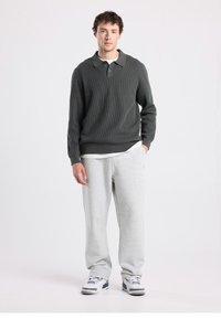 Tummanvihreä ribbineulepusero poolokauluksella. Yhdistetty vaaleanharmaisiin collegehousuihin ja valkoisiin tennareihin, joissa on harmaat ja mustat yksityiskohdat.