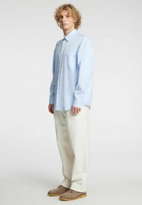 Jasnoniebieska koszula w paski na guziki z kieszenią na piersi, zestawiona z kremowymi spodniami i jasnobrązowymi butami.