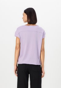 Lavendelkleurig t-shirt met korte mouwen, in een relaxte pasvorm, met een ronde hals en een horizontale naad aan de achterkant. De stof lijkt zacht en lichtgewicht te zijn.
