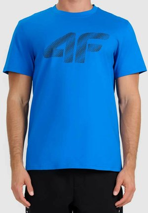 Mężczyzna ubrany w jasnoniebieską koszulkę z krótkim rękawem z czarnym teksturowanym logo "4F" na piersi i czarne spodnie.