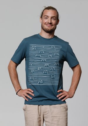 Teal katoenen t-shirt met een witte lijntekening van honden in verschillende poses op de voorkant. Korte mouwen en een ronde hals.
