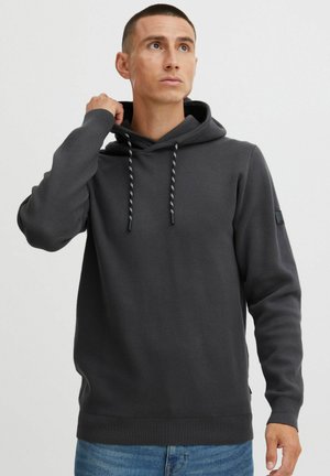 Gray hooded sweatshirt with a drawstring, ribbed cuffs and hem, and a small black patch on the left sleeve. Soft, textured fabric.