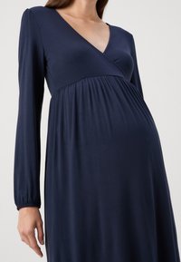 Námořnické těhotenské šaty s hlubokým výstřihem do V, dlouhými rukávy a nařasenou tkaninou pod prsy. Měkký, elastický materiál s hladkým povrchem.