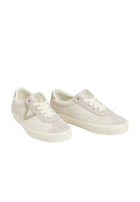 Zapatillas de ante beige con paneles texturizados, cordones de color crema claro y una suela ligeramente elevada. Incluye un logo en la lengüeta y un acento lateral.