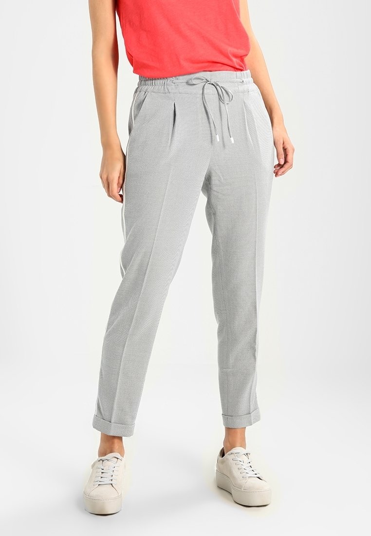 Pantalons gris clair à rayures, dotés d'une taille avec cordon, de plis à l'avant et de manches retroussées, associés à des baskets blanches et un haut rouge.