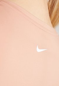 Top deportivo de color rosa claro con textura suave, escote redondeado y logo blanco de Nike en el lado izquierdo cerca del hombro.