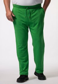 Groene katoenen joggers met een elastische tailleband en trekkoord. Voorzien van zijzakken en ribgebreide cuffs. Gemaakt met zwarte sportschoenen.