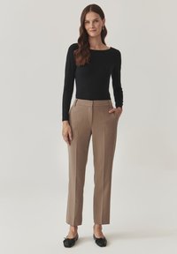 Zwarte lange mouwen top gecombineerd met beige nette broek; de broek heeft zijzakken en een rechte pijp. Zwarte flats maken de outfit compleet.