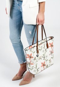 Sac fourre-tout floral avec une surface quiltée blanche, présentant des motifs de fleurs pêches et vertes, des poignées en cuir marron et des accents en métal argenté.