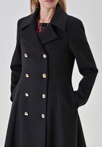 Schwarzer Wollmischmantel mit doppelreihigem Design, großem Kragen und vier goldfarbenen Knöpfen mit glatter Textur.