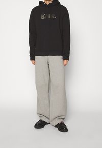 Sudadera negra con el logo "B.A.R." en gris oscuro, combinada con pantalones de chándal de pierna ancha en gris claro y zapatillas negras con suelas texturizadas.
