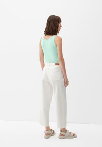 Mintgrünes Tanktop, weiße hoch taillierte Cropped-Hosen mit rohem Saum und beigefarbene Sandalen mit Riemen, von hinten betrachtet.