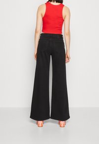 Jeans larges noirs à taille haute, accompagnés d'un débardeur rouge ajusté. Les chaussures sont des talons compensés orange avec des accents de flamme.