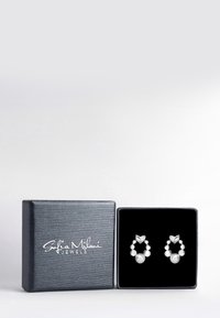 Orecchini in tonalità argento con un design circolare che presenta perle bianche di piccole e grandi dimensioni alternate, esposti in una scatola di gioielli nera e texture.