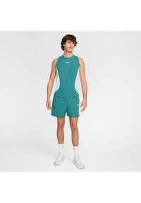 Conjunto atlético en tonos verdosos que incluye una camiseta sin mangas y shorts, con acentos laterales en blanco y un pequeño logo. Fabricado en un tejido suave y transpirable.