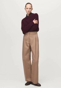 Maglione a maglia borgogna, pantaloni beigi a vita alta e scarpe marroni. I pantaloni presentano pieghe frontali e una vestibilità rilassata. Tessuto dalla superficie liscia.