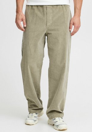 Light olive green corduroy pants with a relaxed fit, elastic waistband, and vertical ribbed texture, paired with white sneakers.