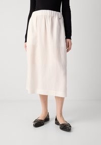 Donna che indossa una gonna bianca midi con vita elastica, scarpe nere con punta e fibbie decorative, e una maglietta nera a maniche lunghe.