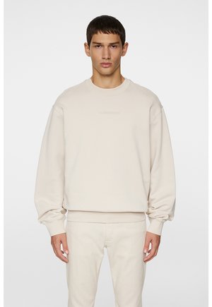 Beige sweatshirt met een ronde hals, verlaagde schouders en ribgebreide boorden. Voorzien van subtiele logo-details op de borst. Zachte stoftextuur.