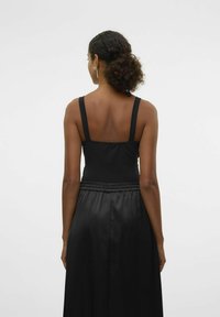 Abito in satin nero con top aderente e spalline regolabili, caratterizzato da una gonna fluida con cintura elastica, visto da dietro.
